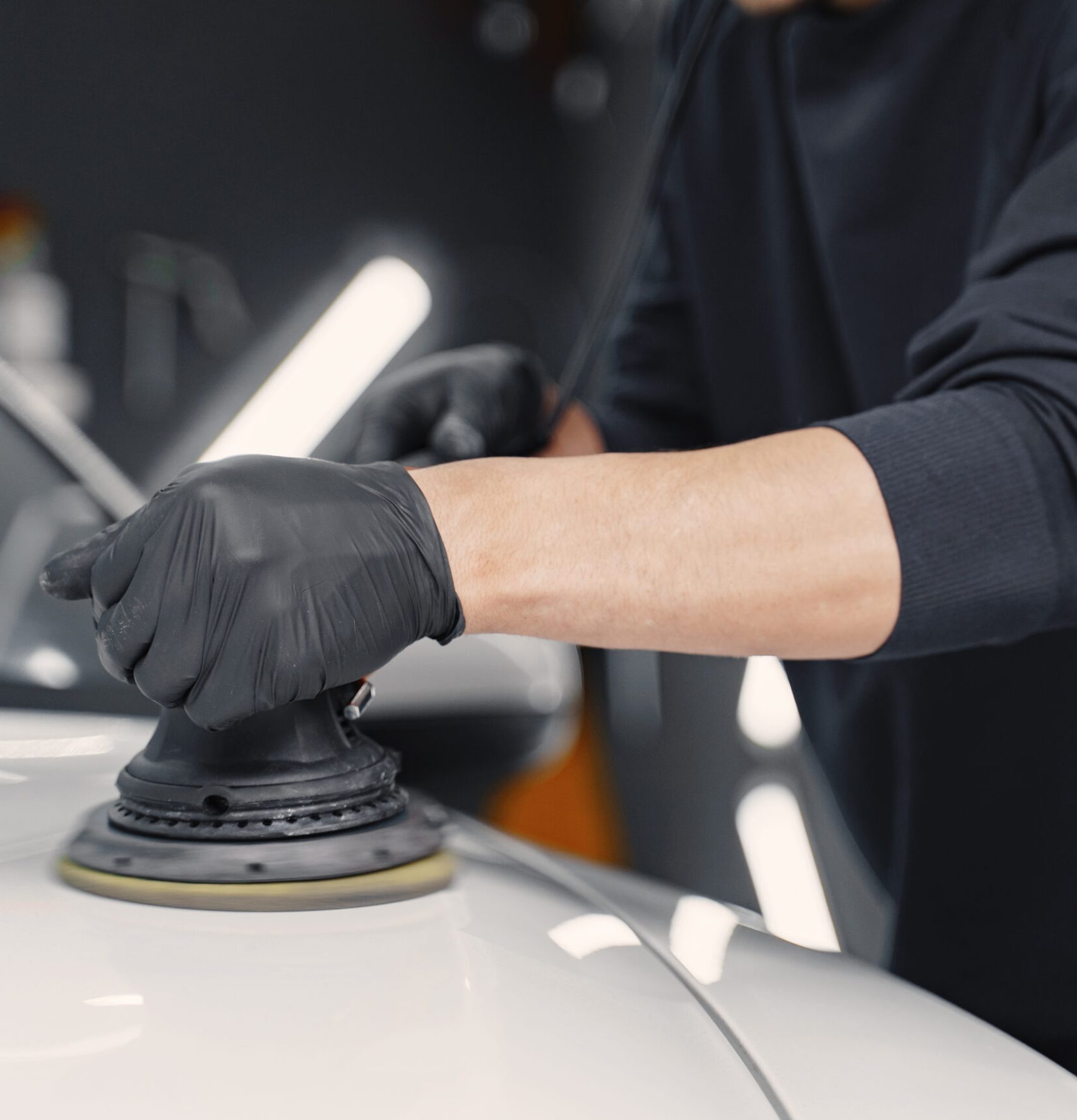 Man in a garage. Worker polish a car. Man in a black uniform.